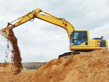 Yellow excavator dumping soil on a construction site.