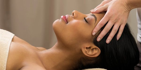 Black woman lying on back having facial muscles massaged by Registered Massage Therapist