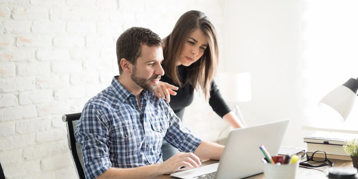 A man and woman collaborating on a laptop in a bright office.