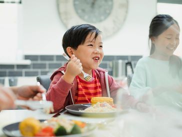 A young boy happily eating corn at a family meal.
