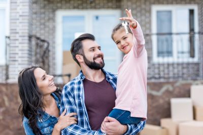 Husband and Wife holding daughter at their new house with keys to the front door.