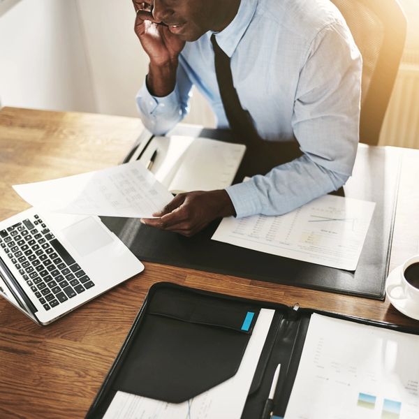 Virtual Assistant working from home at his desk with some papers, an open laptop and cup of coffee.