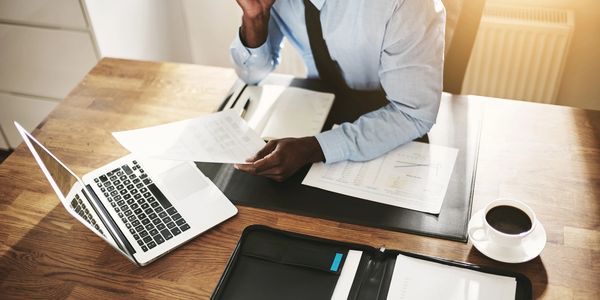 Person reviewing documents at a desk with a laptop and coffee.