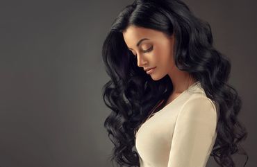 Woman with long, curly black hair looking down thoughtfully.