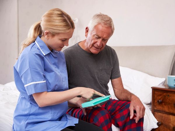 A nurse helping an older man take his medicine