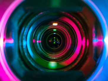 Close-up of a camera lens with vibrant neon reflections.