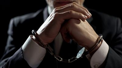 Man in suit with hands cuffed by handcuffs, symbolizing arrest or detention.