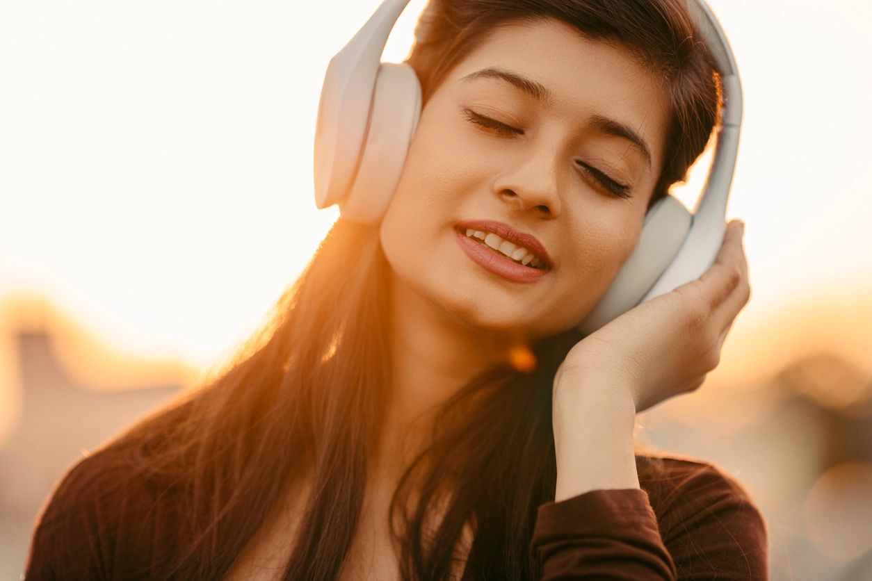 Young woman enjoying music with headphones at sunset.