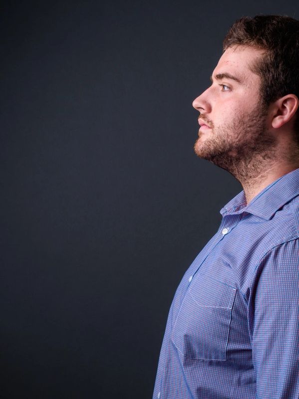 Side profile of a man in a blue shirt against a dark background.
