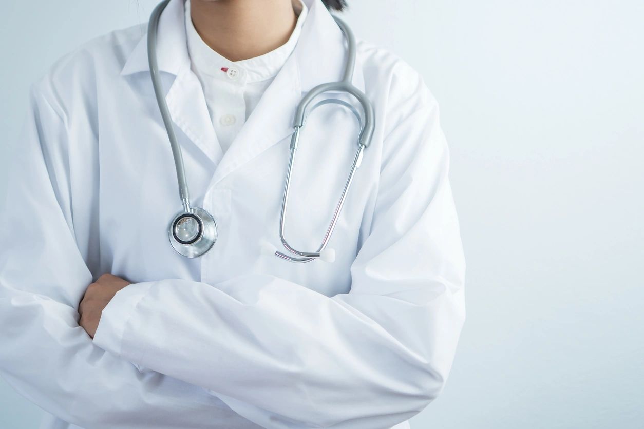 A doctor stands with their arms crossed while in their white coat and a stethoscope around their neck.