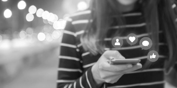 Person holding a smartphone with social media icons floating around.
