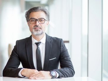 Confident businessman in a suit and glasses sitting at a desk.