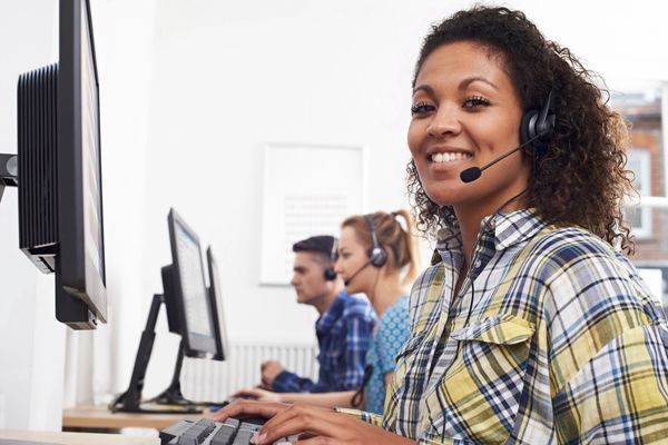 Smiling customer service representative wearing headset at computer.