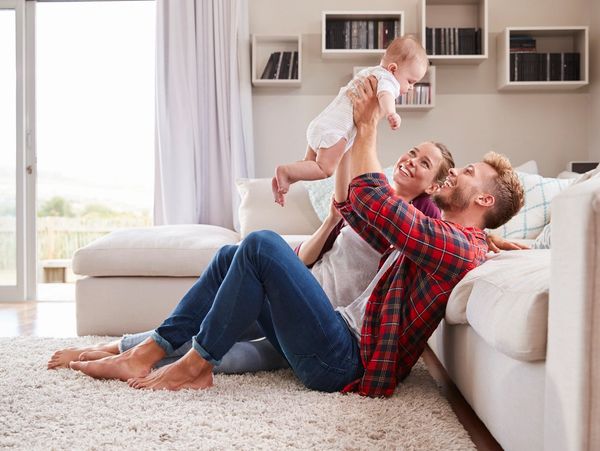 Parents joyfully playing with their baby on the living room floor.