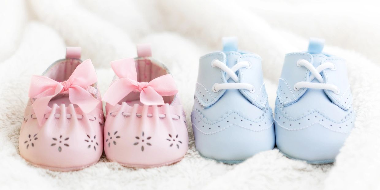 Two pairs of baby shoes, one pink with bows and one blue with laces, on a soft white surface.