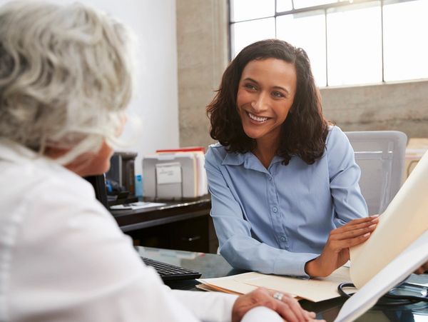 A woman speaking to a client while presenting a document on a desk.