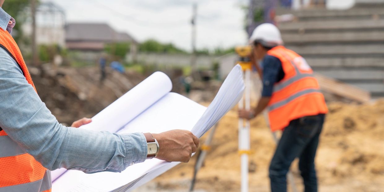 Construction crew using transit and set of blueprints (plans) to survey project.