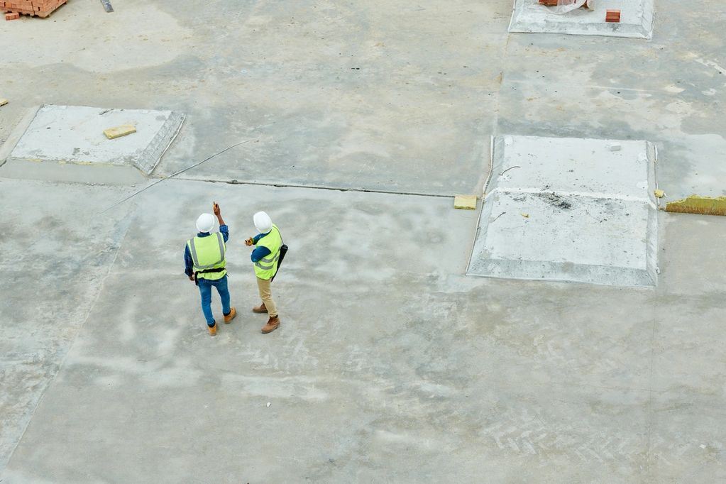 Two construction workers in safety gear inspecting a concrete site.