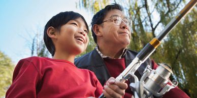 A boy and an older man fishing together outdoors, smiling and enjoying the moment.