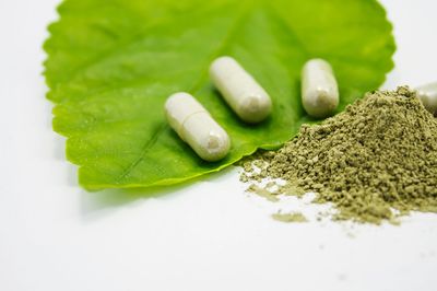 Capsules and herbal powder on a green leaf, symbolizing natural supplements.