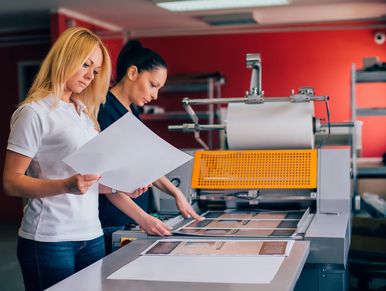 Staff looking at custom printing coming off a printing press.