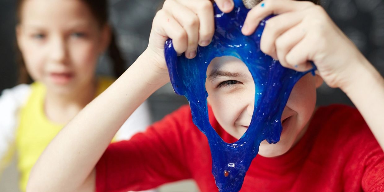 Happy child playing with blue slime in occupational therapy.