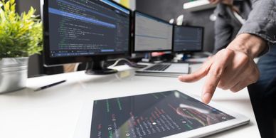 code displayed on 3 monitors and a tablet with a guy at his computer desk working on a website.