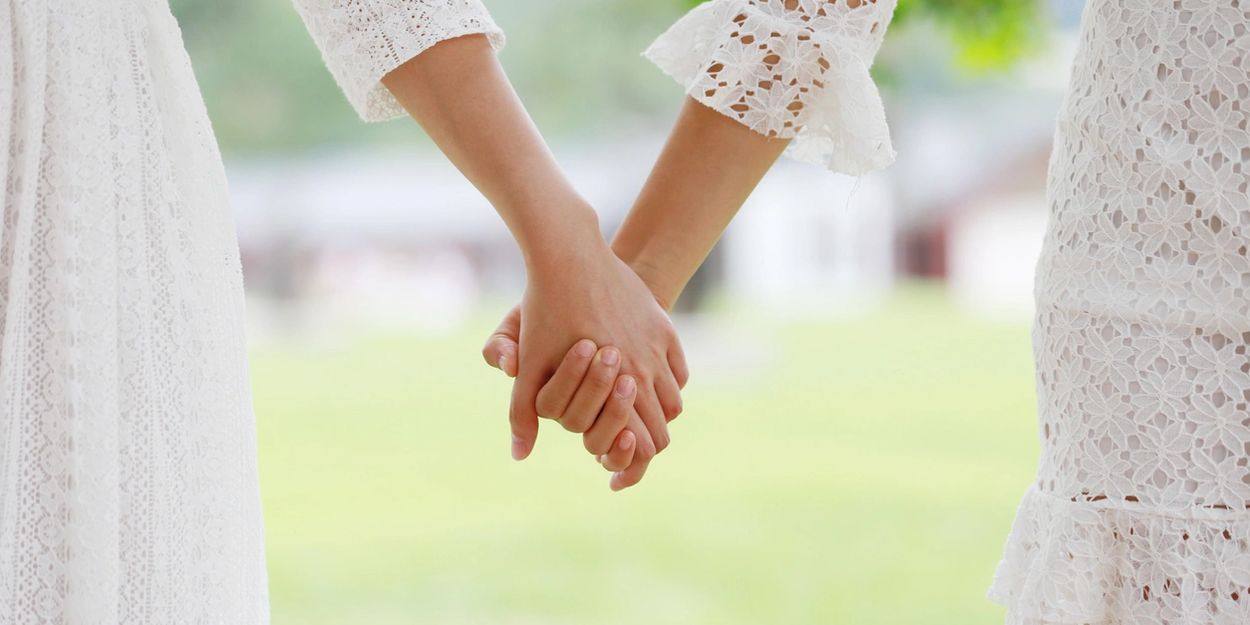 Two people holding hands wearing white lace dresses.