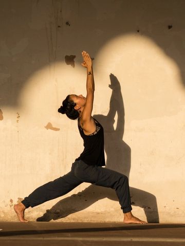 Woman practicing yoga in warrior pose against a sunlit wall.