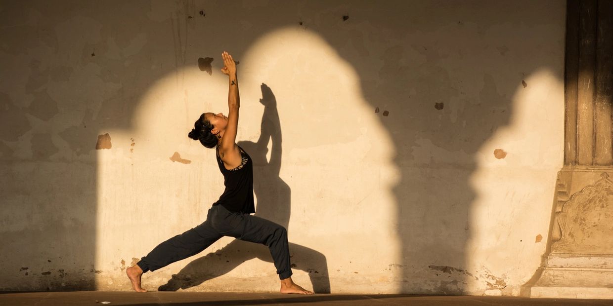 Woman practicing yoga in a graceful warrior pose against a sunlit wall.
