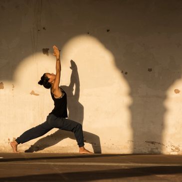 A woman practicing yoga in a graceful pose against a sunlit wall.