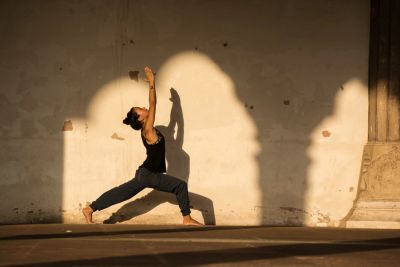 Person practicing yoga in a sunlit area against a textured wall.