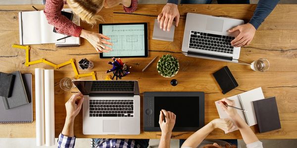 A bird's eye view of a group of employees sitting at a meeting desk with their laptops open.