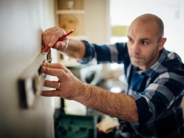 Man measuring a wall with a level tool and pencil.