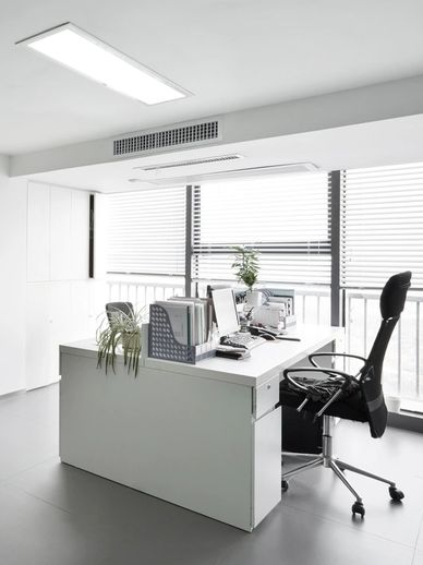 Minimalist white office desk with black ergonomic chair and potted plants near large windows.