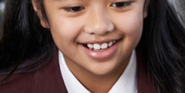 Smiling young girl with dark hair in a school uniform.