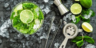 Refreshing mojito with lime, mint, and ice on a dark surface with bartending tools.