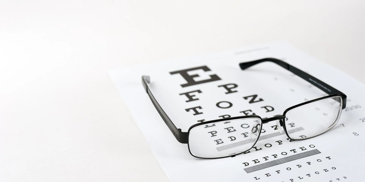 Black-rimmed glasses resting on an eye chart for vision testing.