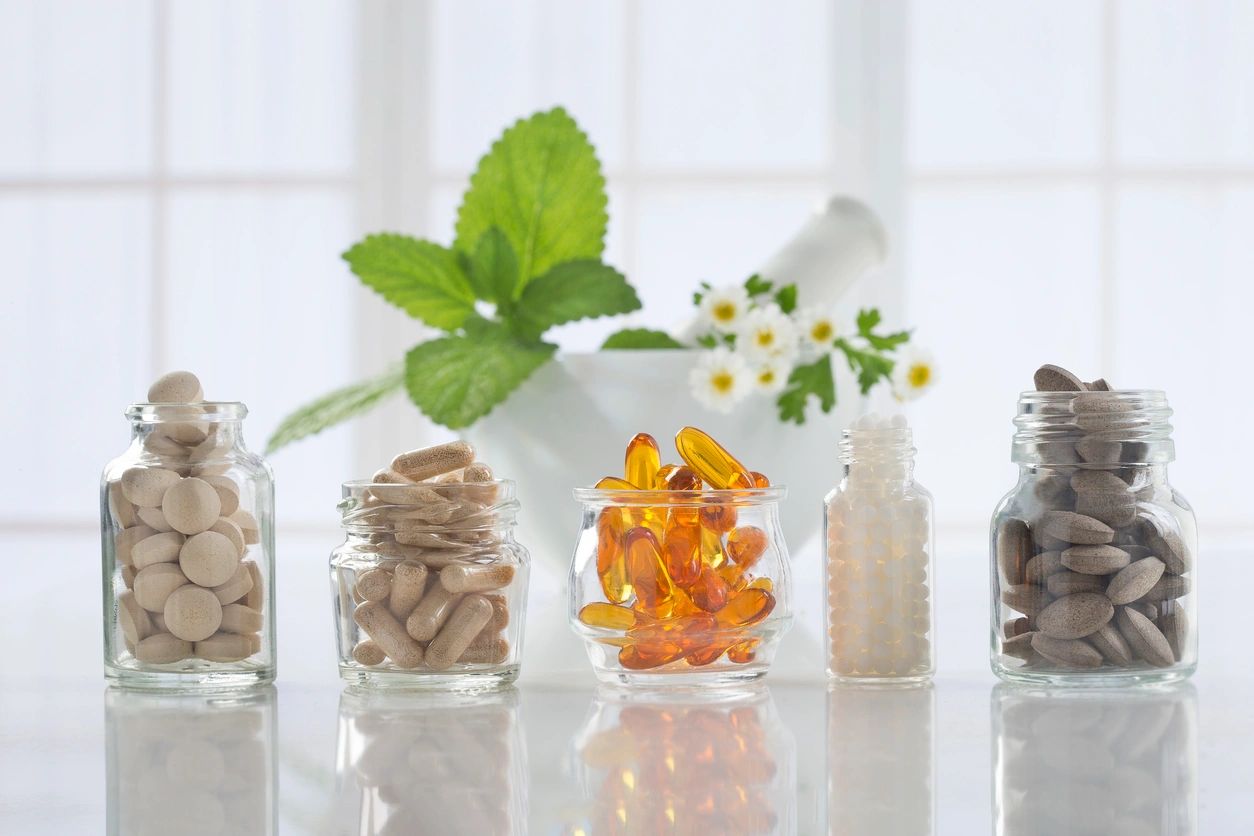 Assorted supplements and vitamins in glass bottles next to fresh green herbs, illustrating the role of antioxidants in immune health.
