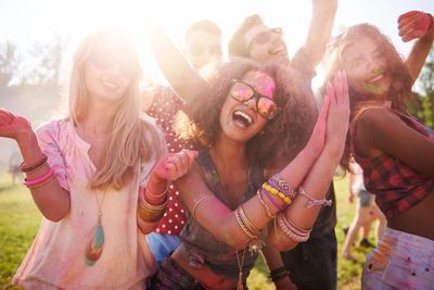Group of friends joyfully celebrating outdoors with colorful powder and bright sunlight.