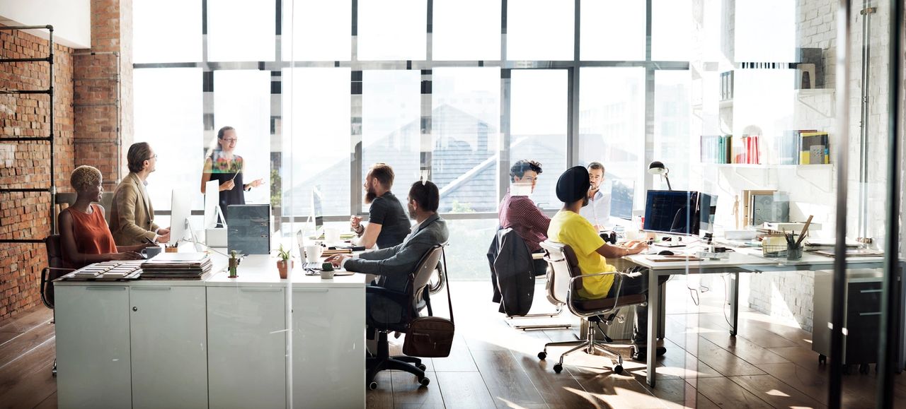 People in the workplace, meeting and working individually, in an open office workspace.