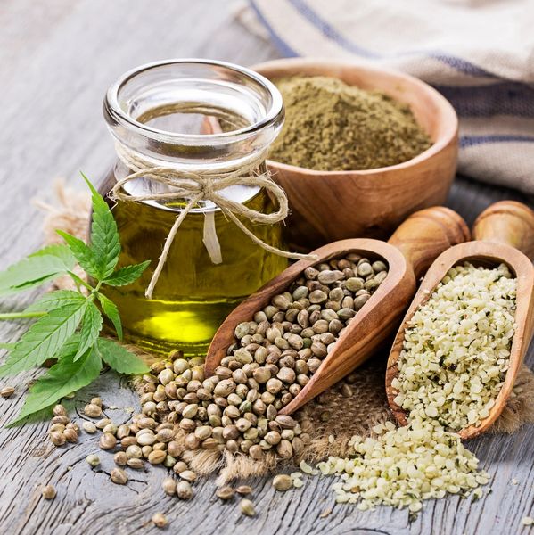 A wooden table with a jar with hemp oil, a scoop with hemp seeds and leaves from a hemp plant