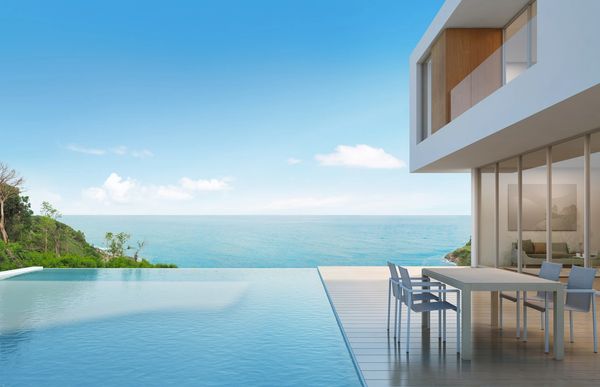 Modern house with infinity pool overlooking the ocean under a clear blue sky.