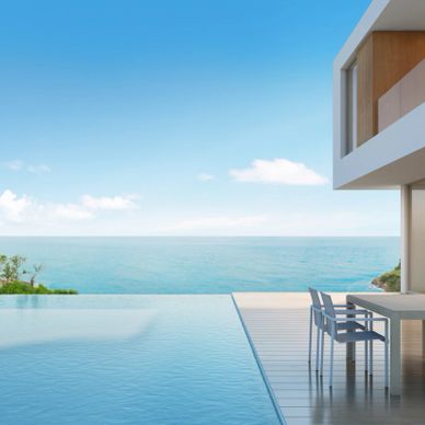 Modern house with an infinity pool overlooking the ocean under a clear blue sky.