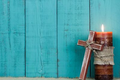 Crucifix leaning on a brown pillar candle wrapped with burlap, against a robin blue planked wall