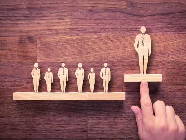 Wooden figures symbolize leadership and promotion in a business hierarchy.