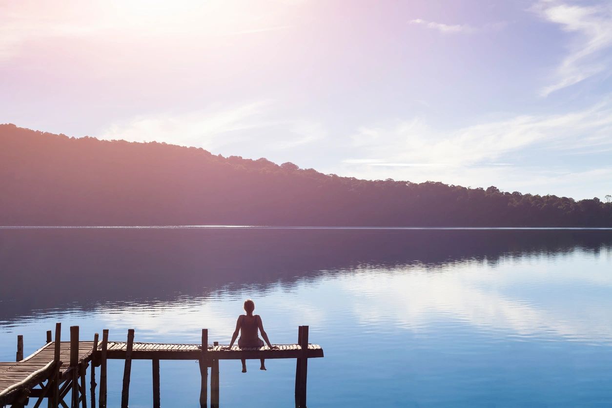 woman sitting on pier at lake