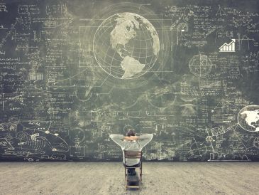 Person sitting and studying a large chalkboard with scientific formulas and globe.