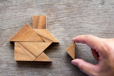 Hand placing a wooden triangle piece to complete a house shape puzzle.
