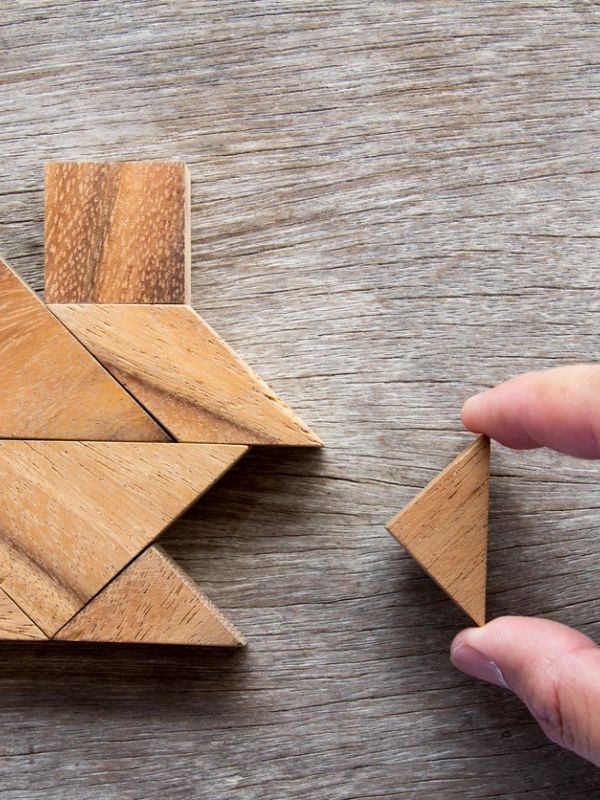 Hand holding a wooden triangle puzzle piece.